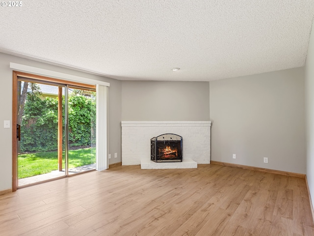 619 SE 121st Ave Unit 23, Vancouver, WA 98683 - unfurnished living room featuring a brick fireplace, light wood-style flooring, a textured ceiling, and baseboards