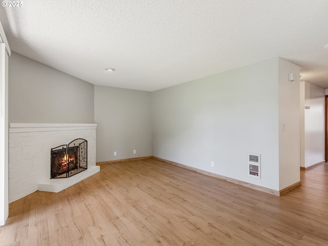 619 SE 121st Ave Unit 23, Vancouver, WA 98683 - unfurnished living room featuring heating unit, a fireplace, a textured ceiling, light wood-style floors, and baseboards