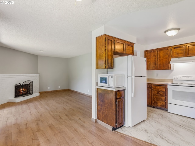 619 SE 121st Ave Unit 23, Vancouver, WA 98683 - kitchen featuring white appliances, under cabinet range hood, a textured ceiling, a fireplace, and brown cabinetry