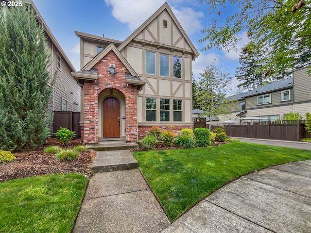 english style home featuring brick siding, stucco siding, a front yard, and fence