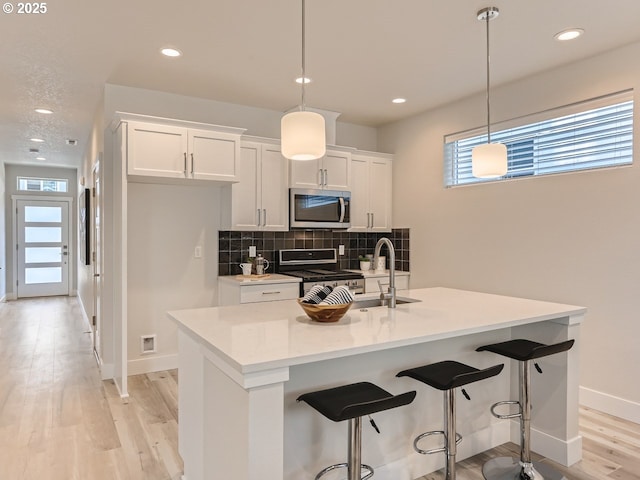 kitchen featuring pendant lighting, stainless steel appliances, a kitchen island with sink, and white cabinets