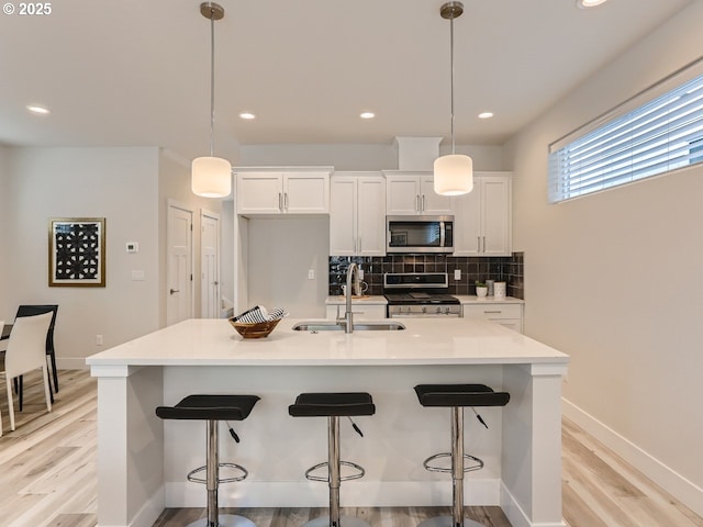 kitchen with an island with sink, appliances with stainless steel finishes, decorative light fixtures, and sink