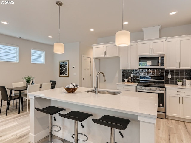 kitchen featuring appliances with stainless steel finishes, decorative light fixtures, sink, and a center island with sink