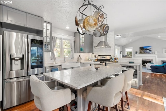 kitchen with stainless steel appliances, light wood-type flooring, a sink, and wall chimney range hood