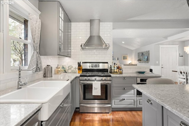 kitchen with gray cabinetry, vaulted ceiling, backsplash, wall chimney exhaust hood, and gas range