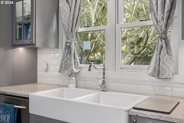 kitchen with tasteful backsplash, glass insert cabinets, gray cabinets, and a sink