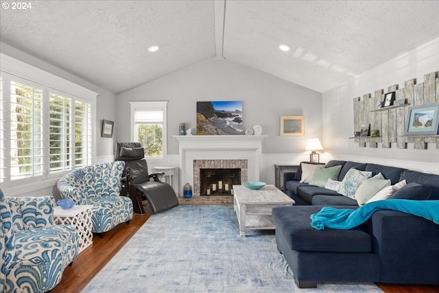 living area featuring lofted ceiling, a textured ceiling, a fireplace, wood finished floors, and wainscoting