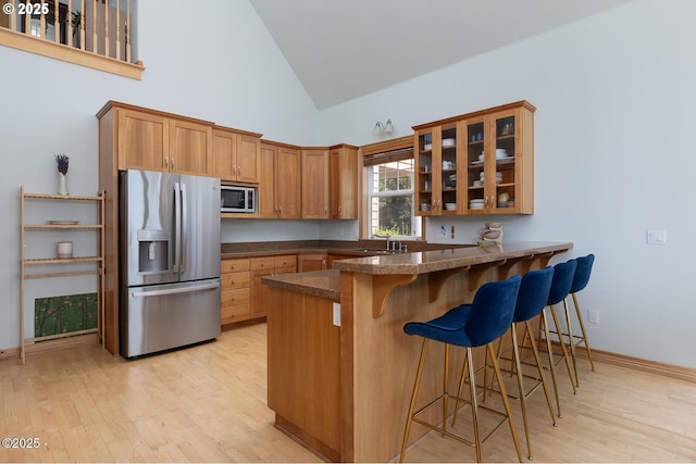 5340 Haystack Dr, Neskowin, OR 97149 - kitchen with appliances with stainless steel finishes, high vaulted ceiling, glass insert cabinets, a peninsula, and light wood-style flooring