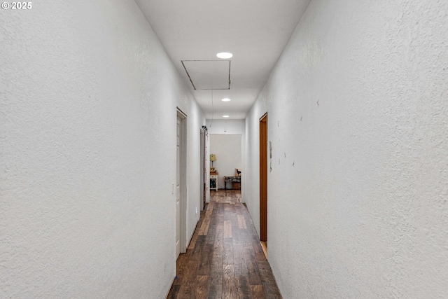 corridor with recessed lighting, a textured wall, attic access, and dark wood-type flooring