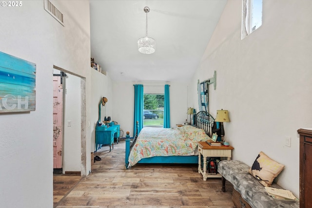 bedroom featuring high vaulted ceiling, visible vents, a barn door, and wood finished floors
