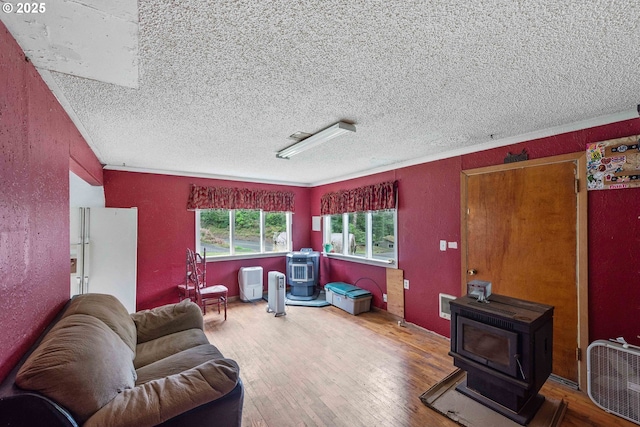 interior space featuring a textured ceiling, a textured wall, wood finished floors, and a wood stove