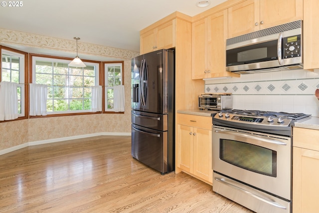 kitchen with light brown cabinetry, light wood-type flooring, light countertops, stainless steel appliances, and wallpapered walls