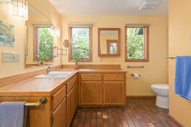bathroom with toilet, a wealth of natural light, brick floor, and vanity