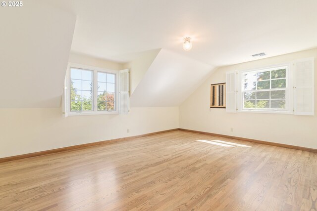 additional living space featuring baseboards, plenty of natural light, lofted ceiling, and light wood-type flooring