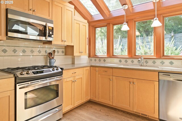 kitchen featuring decorative backsplash, a skylight, appliances with stainless steel finishes, a sink, and light countertops