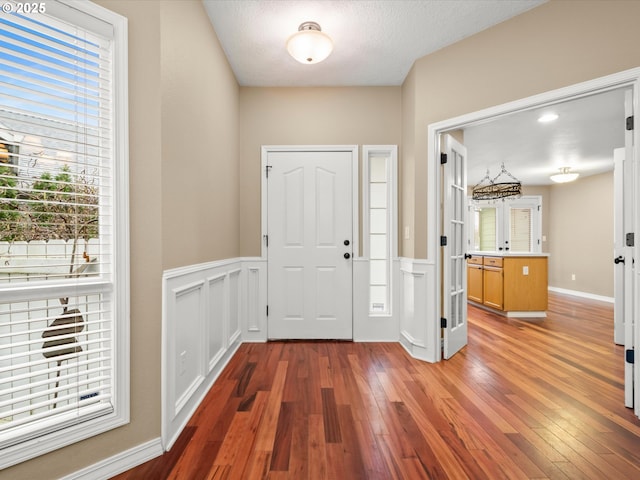 foyer with wood-type flooring, a wainscoted wall, a decorative wall, and a textured ceiling