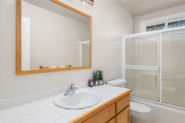 full bathroom featuring vanity, bath / shower combo with glass door, and toilet