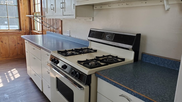 kitchen featuring dark countertops, gas range gas stove, dark wood finished floors, wooden walls, and white cabinetry