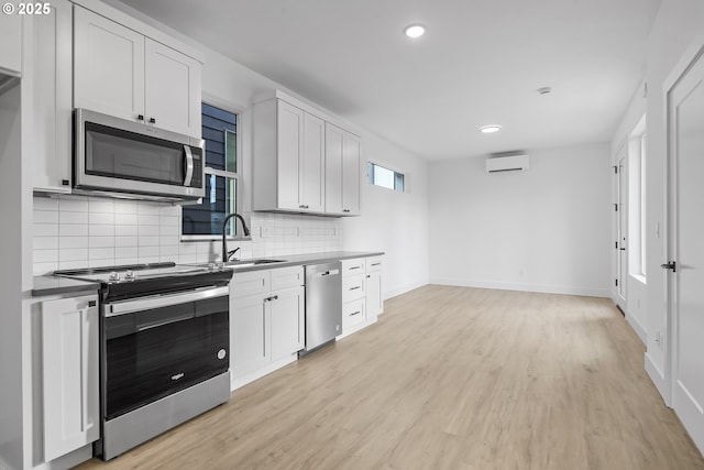 kitchen featuring appliances with stainless steel finishes, sink, a wall mounted AC, white cabinets, and light hardwood / wood-style flooring