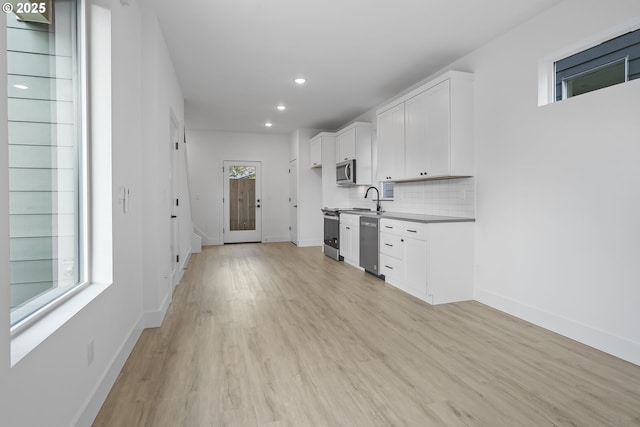 kitchen with stainless steel appliances, white cabinetry, tasteful backsplash, and light hardwood / wood-style floors