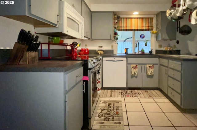 kitchen featuring a sink, light tile patterned flooring, dark countertops, and white appliances