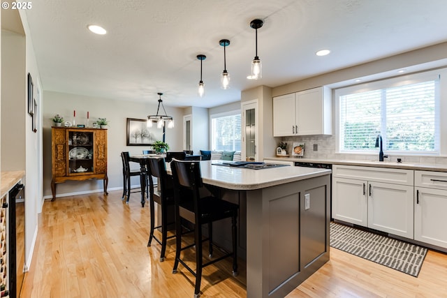 kitchen featuring a center island, a sink, light countertops, light wood-style floors, and white cabinetry