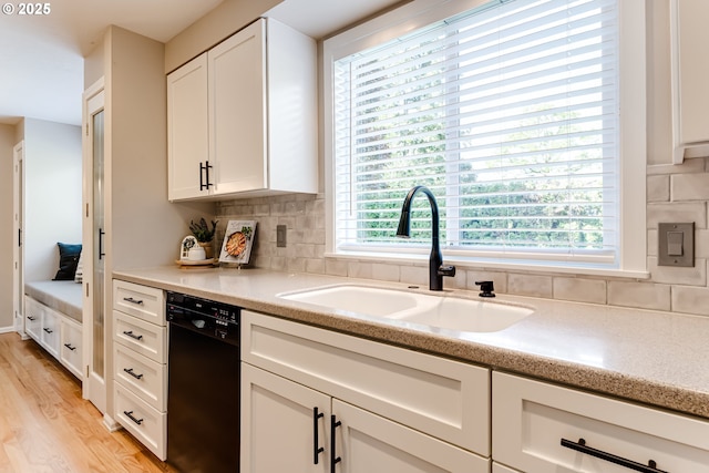 kitchen with white cabinets, a sink, light wood finished floors, black dishwasher, and tasteful backsplash