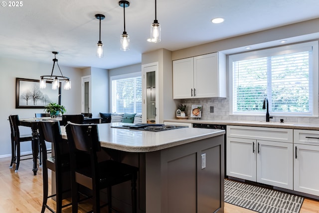 kitchen with a sink, a kitchen island, black stovetop, and a wealth of natural light