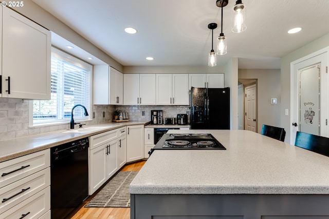 kitchen featuring a kitchen island, light wood-style floors, light countertops, a sink, and black appliances