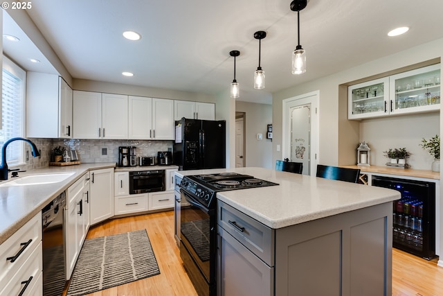 kitchen with a sink, light countertops, black appliances, and beverage cooler