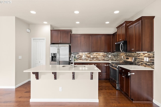 kitchen with appliances with stainless steel finishes, a sink, dark wood-type flooring, a kitchen island with sink, and decorative backsplash