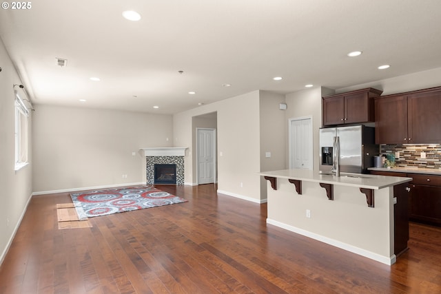 kitchen with stainless steel refrigerator with ice dispenser, dark wood-style floors, light countertops, a kitchen bar, and recessed lighting