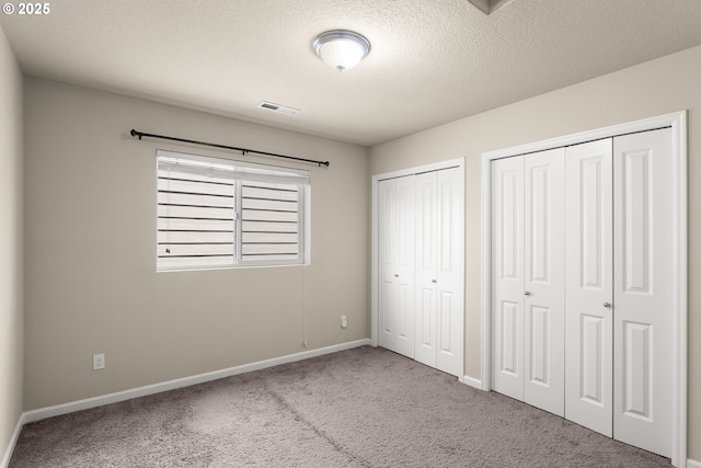 unfurnished bedroom featuring carpet floors, two closets, baseboards, and a textured ceiling