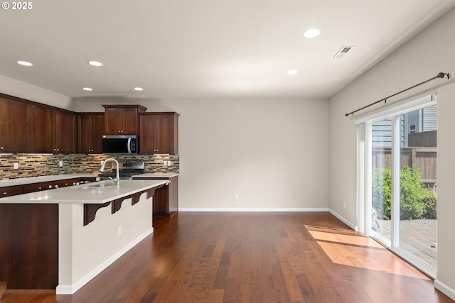 kitchen featuring stainless steel appliances, light countertops, a sink, backsplash, and a breakfast bar area