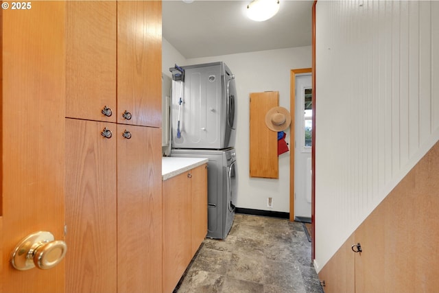 laundry area featuring stacked washer / drying machine, cabinet space, and baseboards