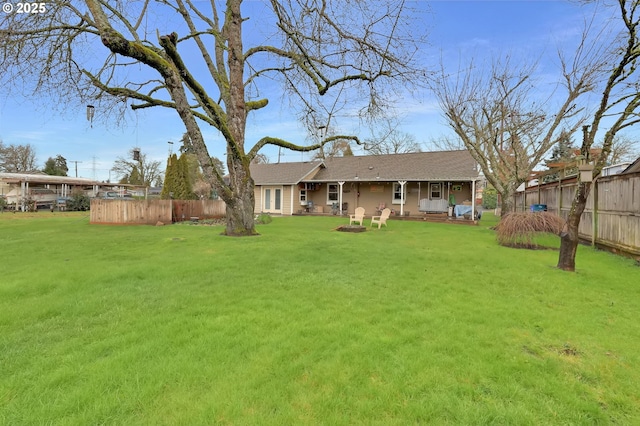 back of house with an outdoor fire pit, fence, and a yard