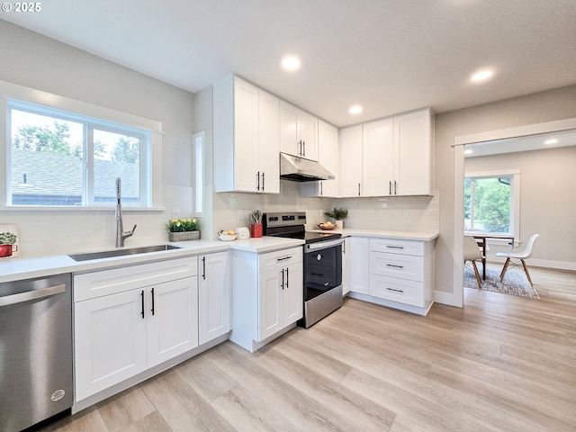14127 SE Center St, Portland, OR 97236 - kitchen featuring appliances with stainless steel finishes, under cabinet range hood, light countertops, white cabinets, and light wood-type flooring