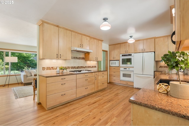 kitchen featuring light brown cabinets, white appliances, a sink, light wood-type flooring, and tasteful backsplash
