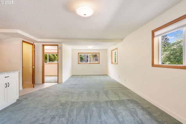 spare room with light carpet, a textured ceiling, and baseboards