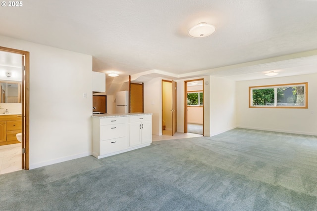 unfurnished bedroom with freestanding refrigerator, light carpet, baseboards, and ensuite bathroom