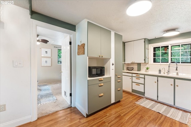 2906 SW Spring Garden St, Portland, OR 97219 - kitchen featuring black microwave, light wood-type flooring, light countertops, a sink, and a textured ceiling