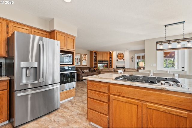 kitchen with open floor plan, light countertops, brown cabinets, decorative light fixtures, and stainless steel appliances
