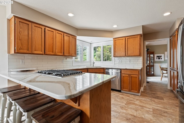 kitchen featuring a kitchen breakfast bar, appliances with stainless steel finishes, brown cabinets, a sink, and a peninsula