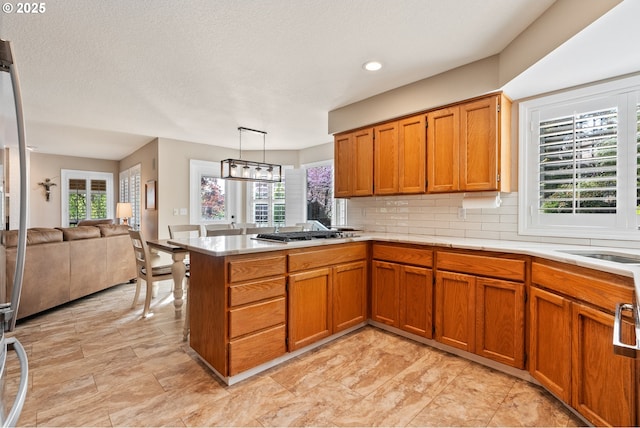kitchen with brown cabinetry, light countertops, a peninsula, and a wealth of natural light
