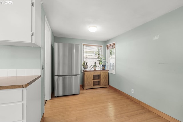 kitchen featuring freestanding refrigerator, light wood-type flooring, white cabinetry, and baseboards