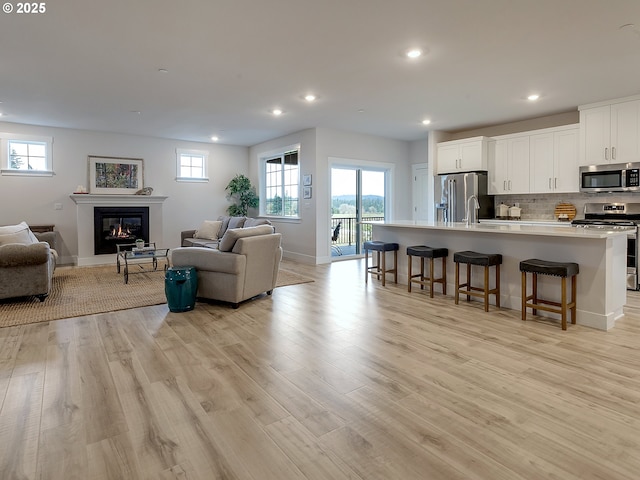 living room featuring recessed lighting, a glass covered fireplace, a healthy amount of sunlight, and light wood finished floors
