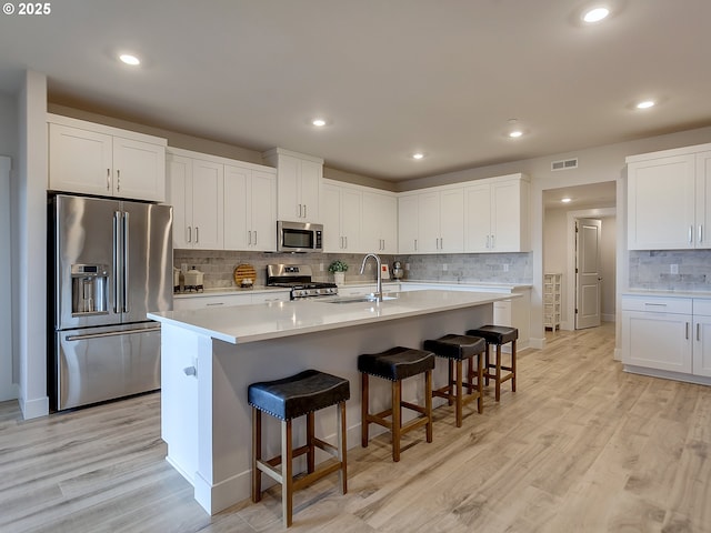 kitchen featuring a sink, light wood finished floors, backsplash, appliances with stainless steel finishes, and visible vents