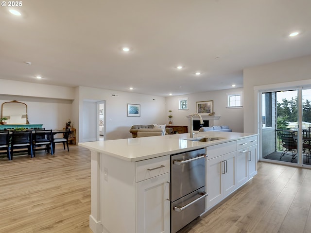 kitchen with a sink, open floor plan, a center island with sink, light wood-style flooring, and recessed lighting