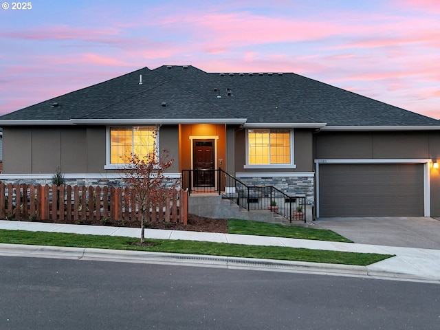 view of front of home featuring a fenced front yard, roof with shingles, concrete driveway, a garage, and stone siding