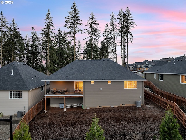 back of house at dusk featuring a wooden deck, a fenced backyard, and central air condition unit